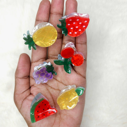 Hand holding colorful fruit-shaped acrylic hair claw clips against a white background