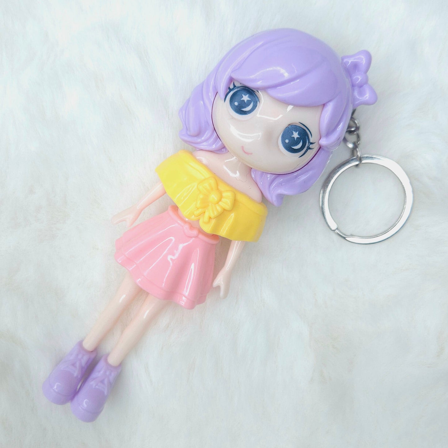 Keychain in the shape of a doll with purple hair and a yellow top on a white background