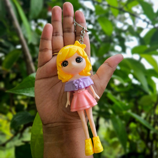 Hand holding a small doll-shaped keychain with a blurred green leafy background