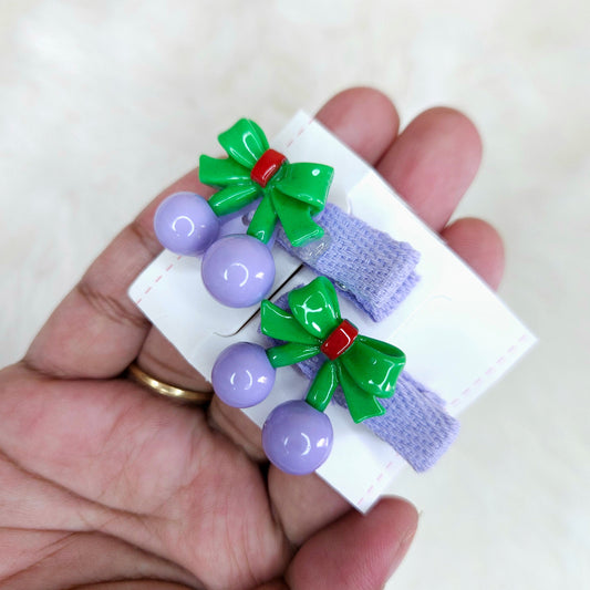 Set of hair accessories with green bows and purple beads on a white card held by a hand.