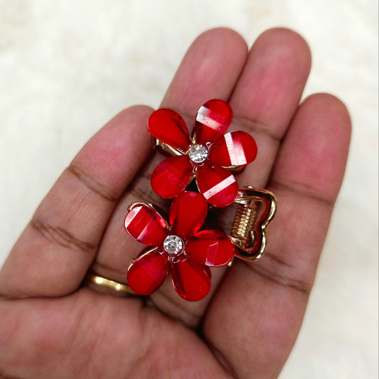 Red flower-shaped hair clip with gold accents held in a hand against a white background