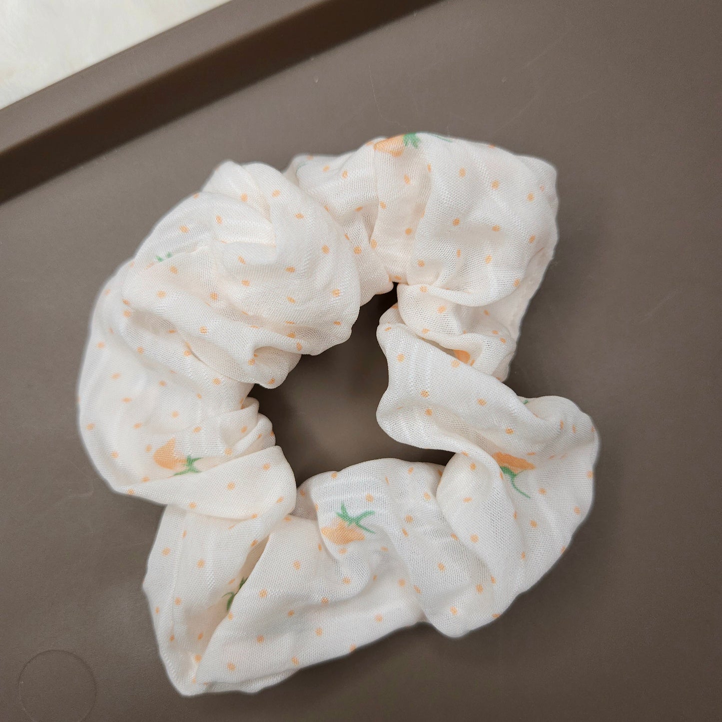 White scrunchie with small prints and orange flowers on a brown surface