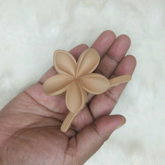 Hand holding a beige flower-shaped hair claw against a white background