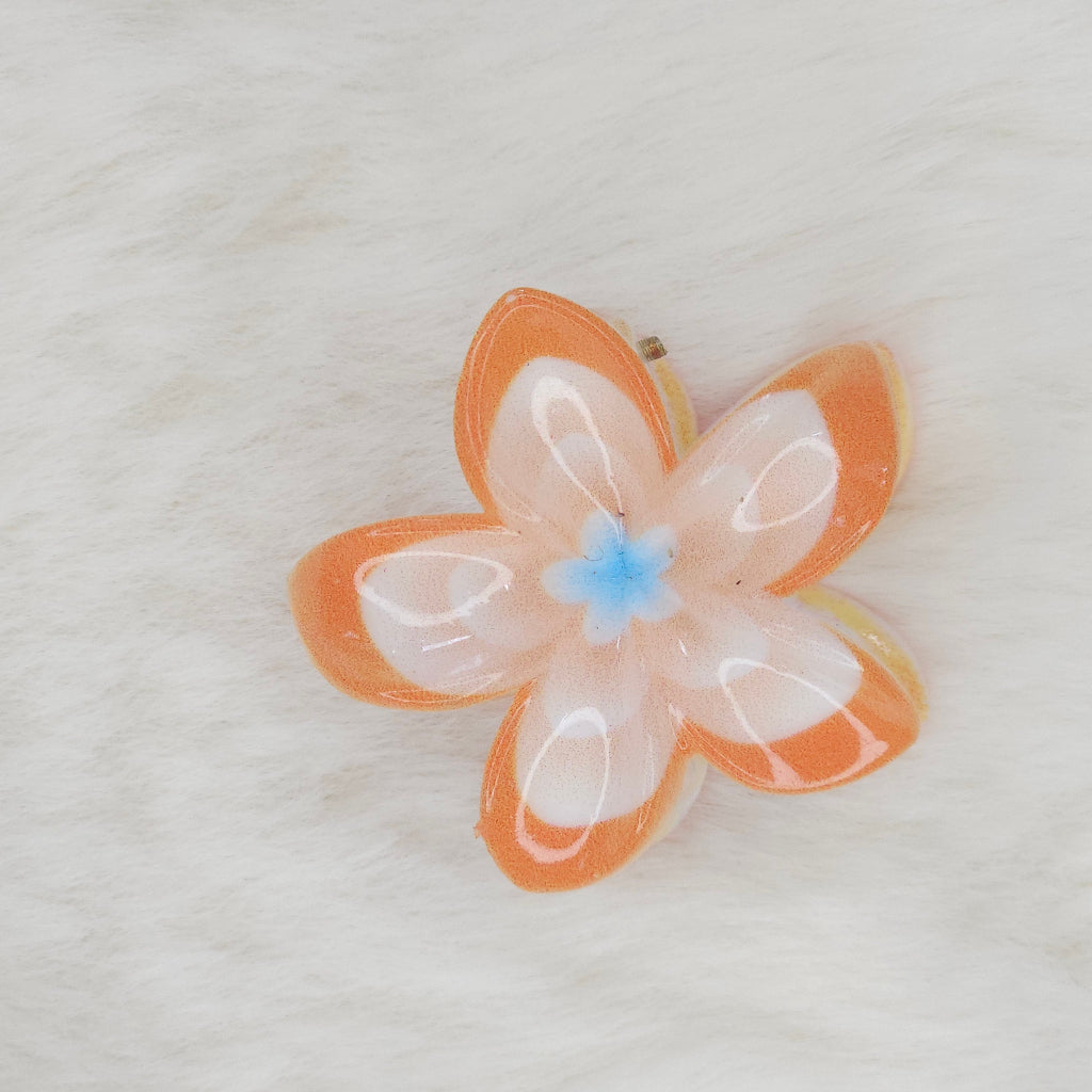 A yellow and white translucent plastic flower-shaped hair clip with a light yellow center, seen from above.