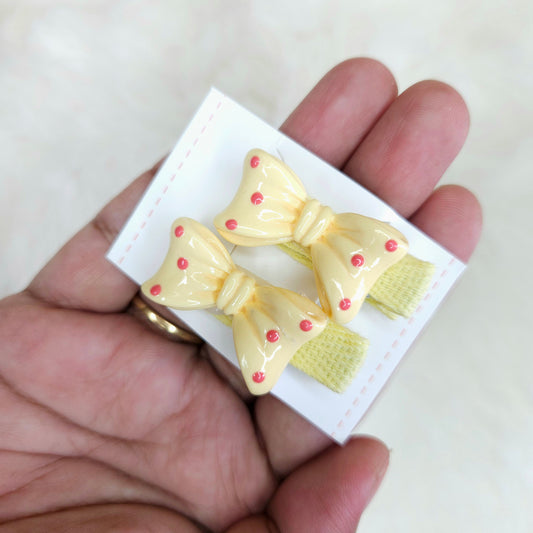 Two yellow bow-shaped hair clips with red centers on a white card held by a hand.
