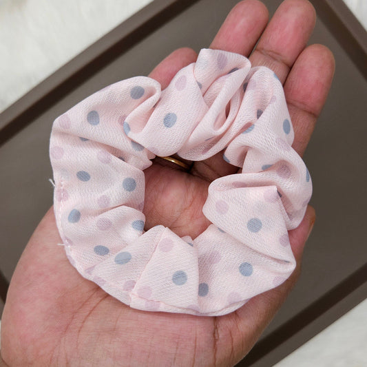 Pink scrunchie with blue dots held in a hand against a neutral background