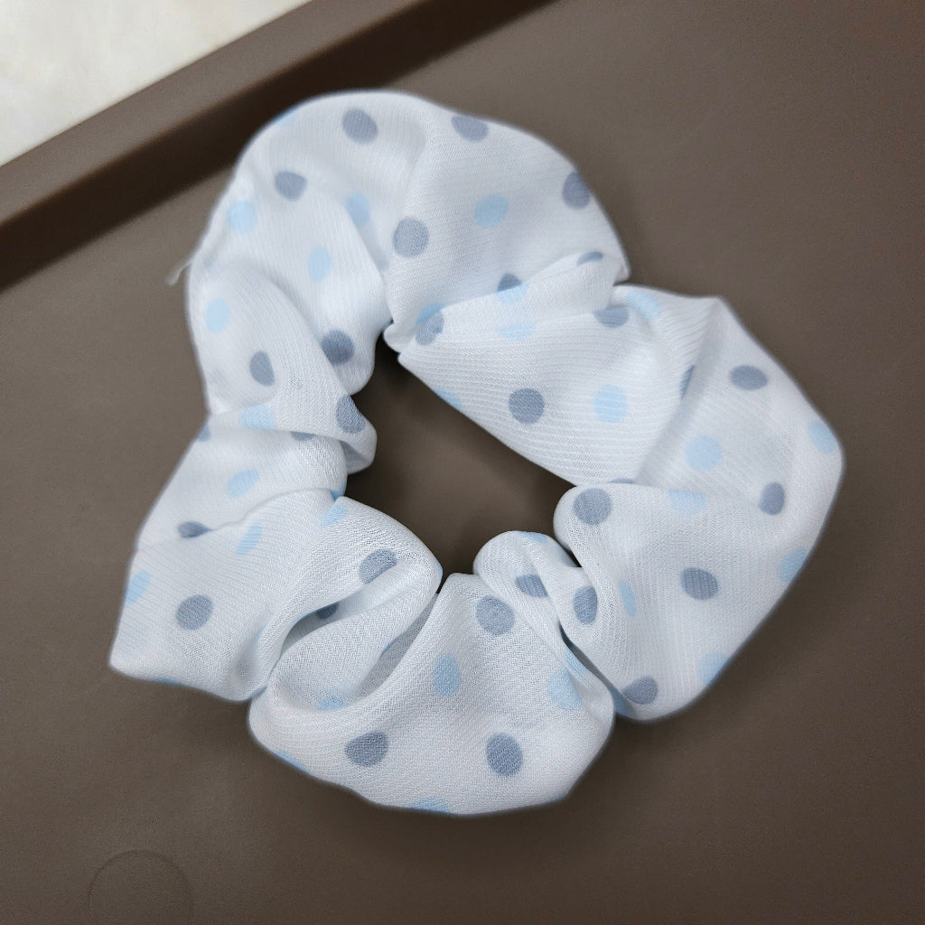 White scrunchie with blue polka dots on a dark surface