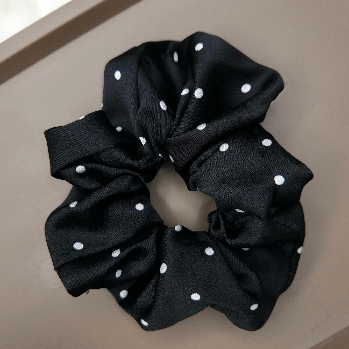 Black scrunchie with white polka dots on a beige surface