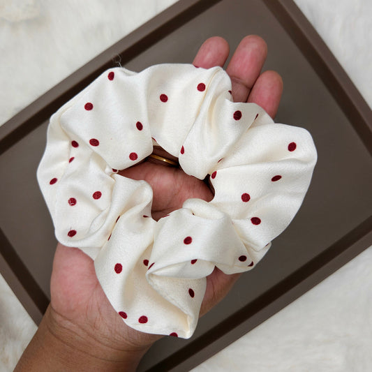 White scrunchie with red polka dots held in a hand on a neutral background