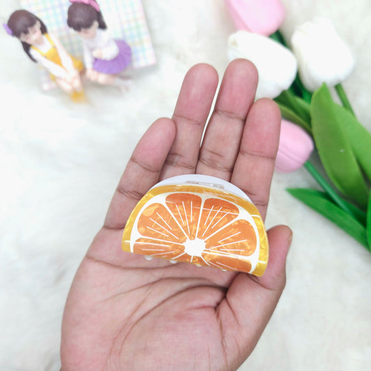 Hand holding a round hair claw with a blurred background of flowers and figurines.