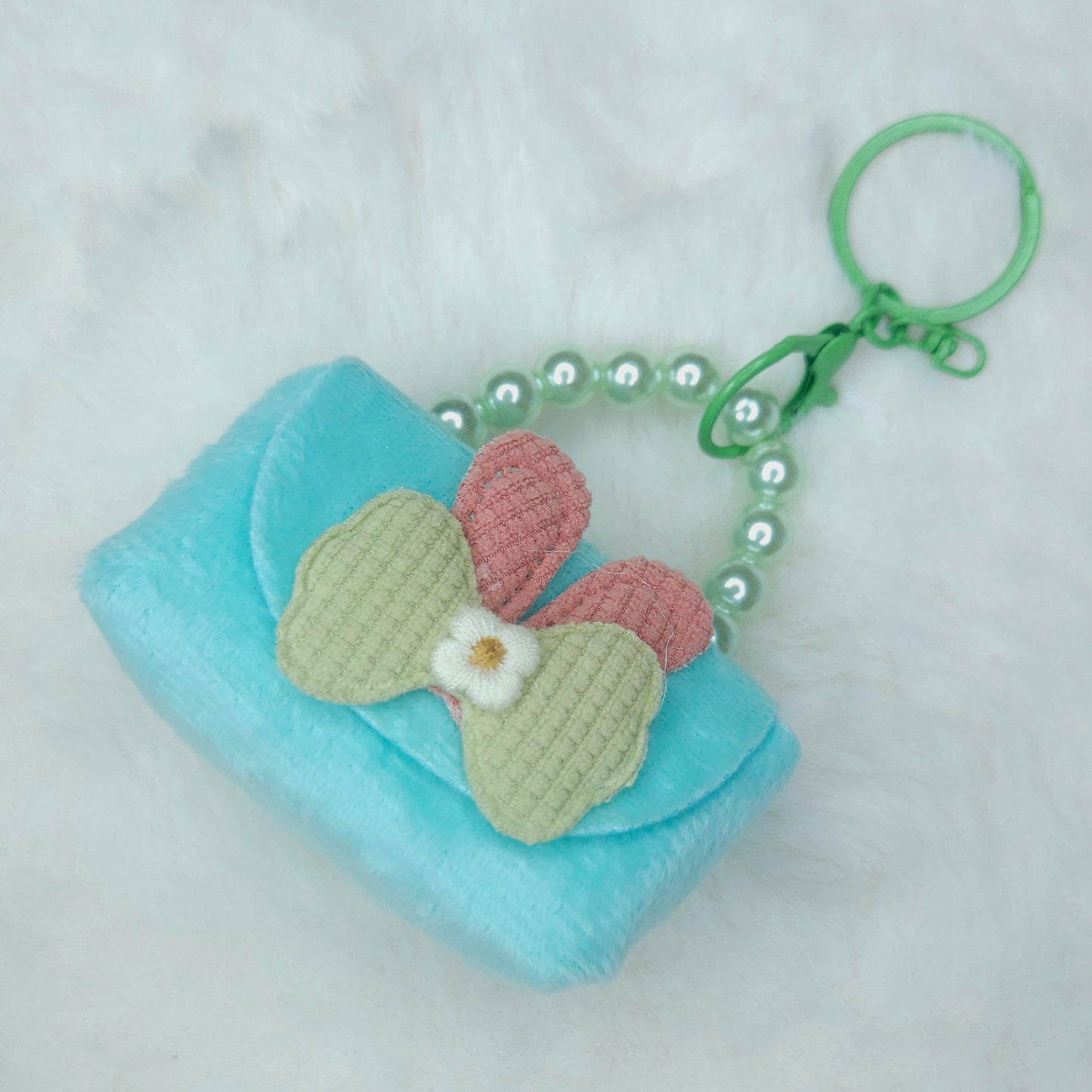 Small turquoise pouch with a pink and green butterfly charm on a white background