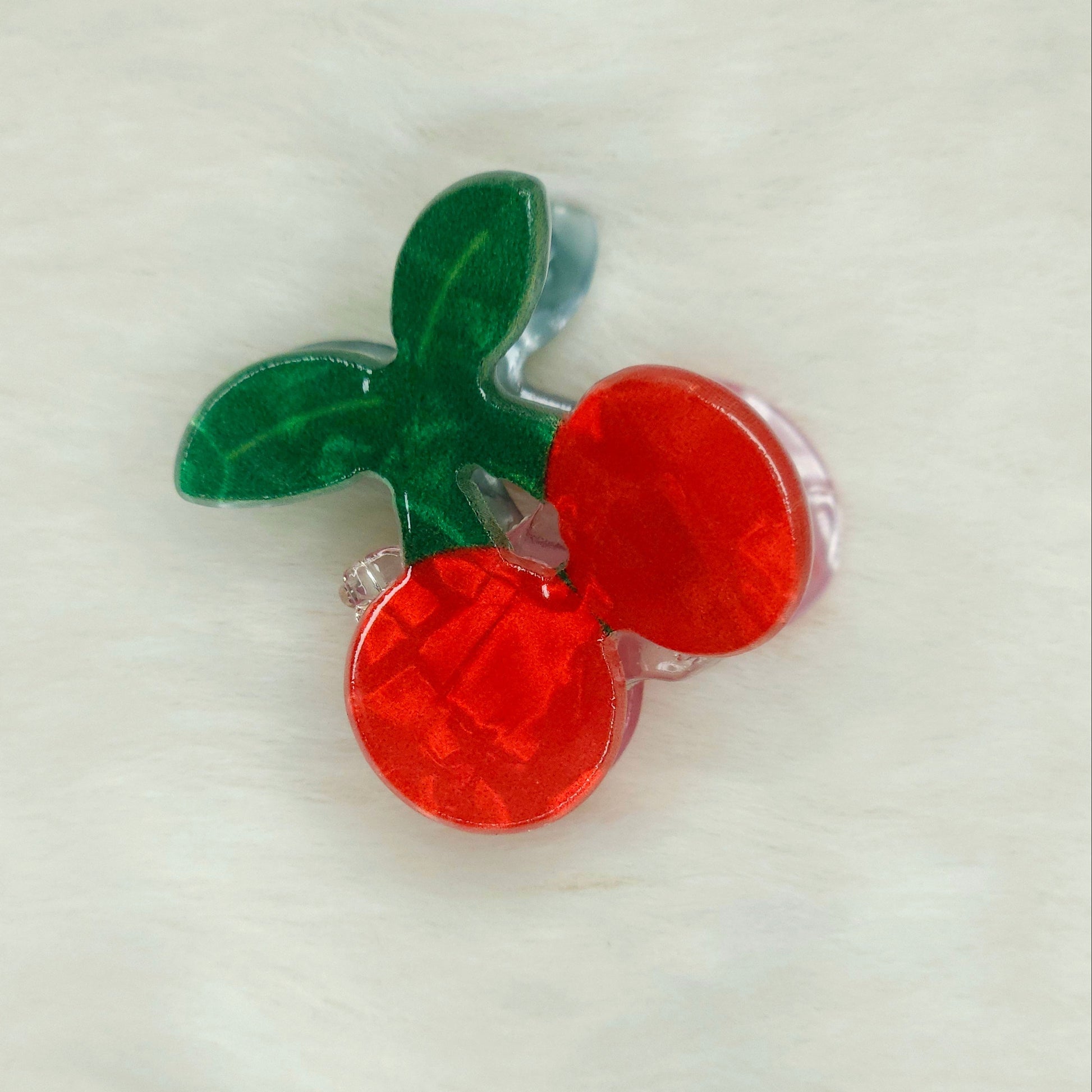 Red and green cherry acrylic hair claw clip on a white background