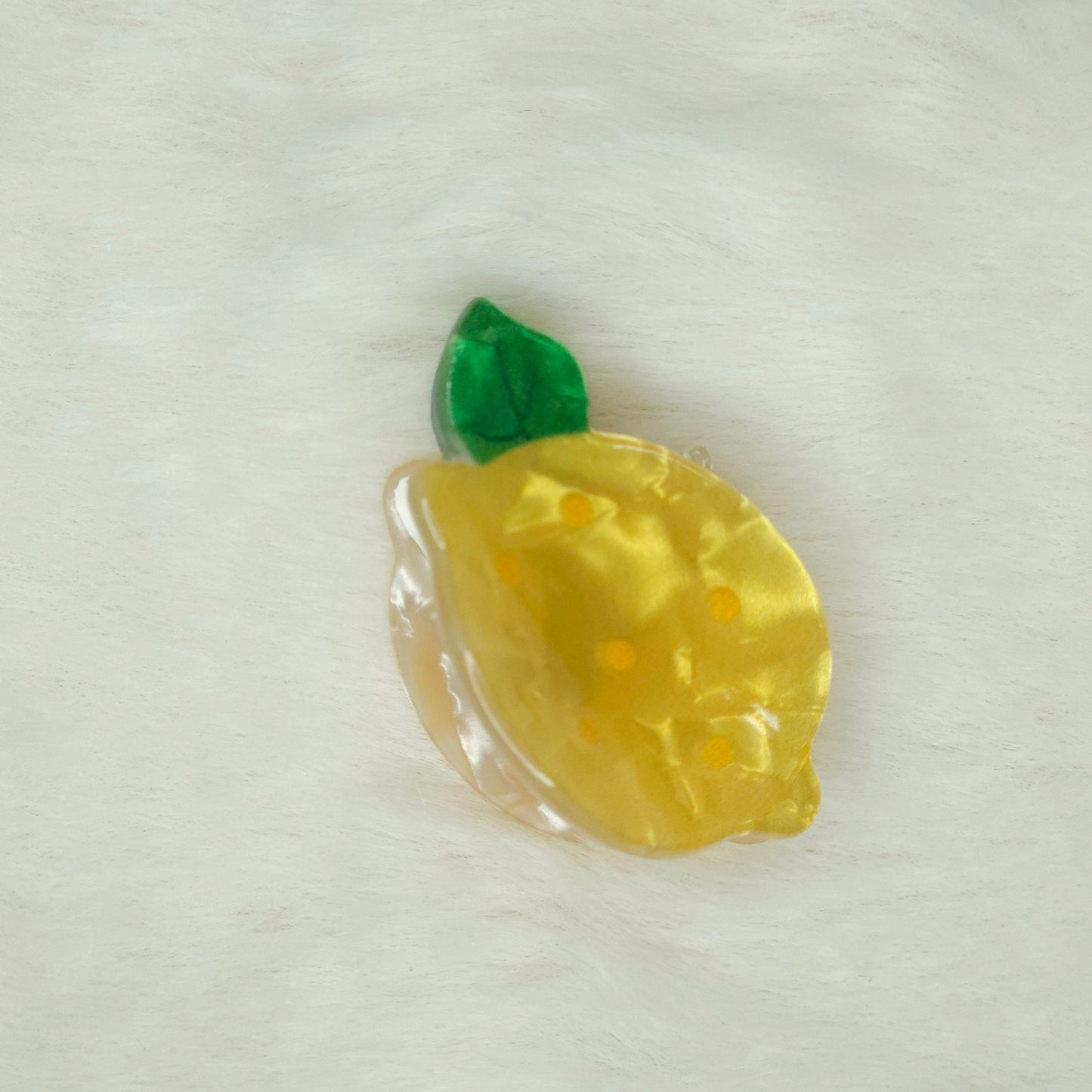 Yellow lemon-shaped hair claw clip with a green leaf on a white background