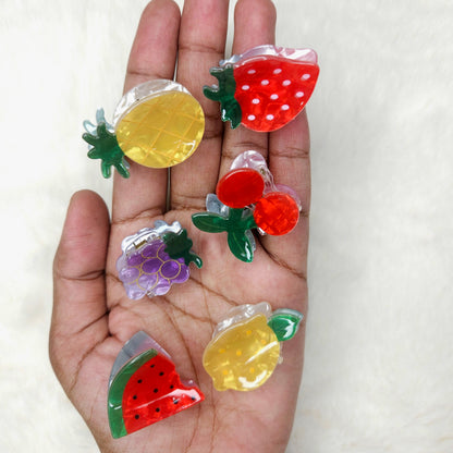 Hand holding colorful fruit-shaped acrylic hair claw clips against a white background