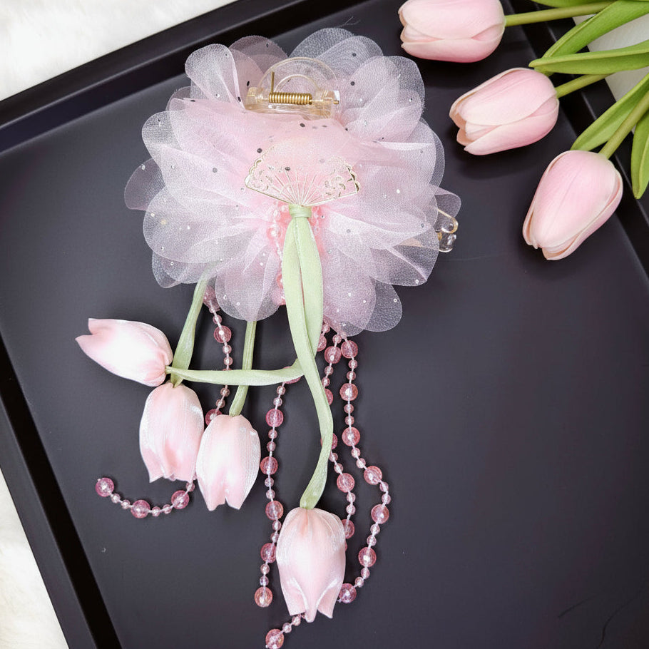 Decorative hair accessory with pink flowers and beads on a black tray with tulips.
