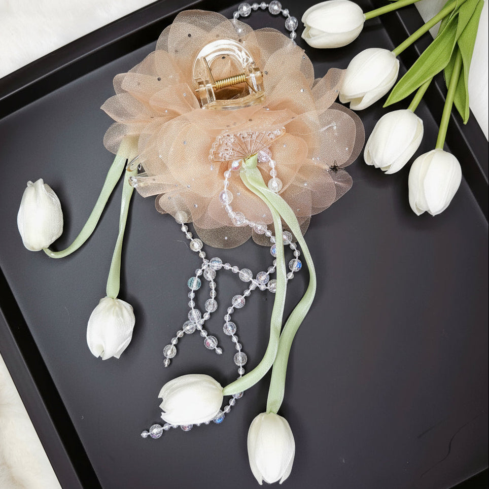 Decorative hair claw clip with flowers and beads on a black tray with white tulips.
