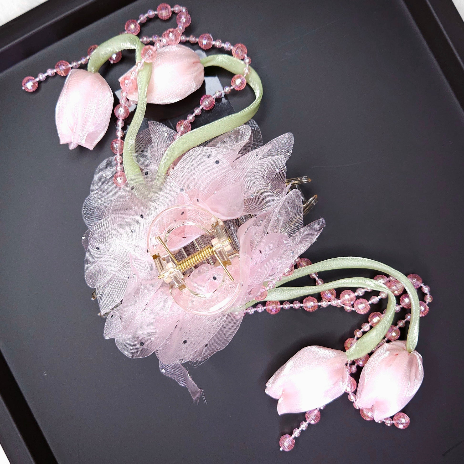 Decorative hair clip with pink flowers and beads on a black tray