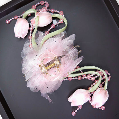 Decorative hair clip with pink flowers and beads on a black tray