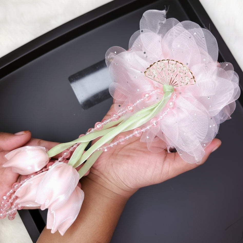 Hand holding a decorative flower claw with pink petals and a sheer white center on a dark surface.