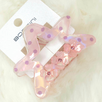 Pink butterfly hair clip with floral details on a white background