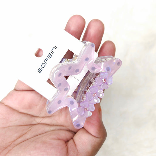 Hand holding a decorative hair clip with floral details on a white background