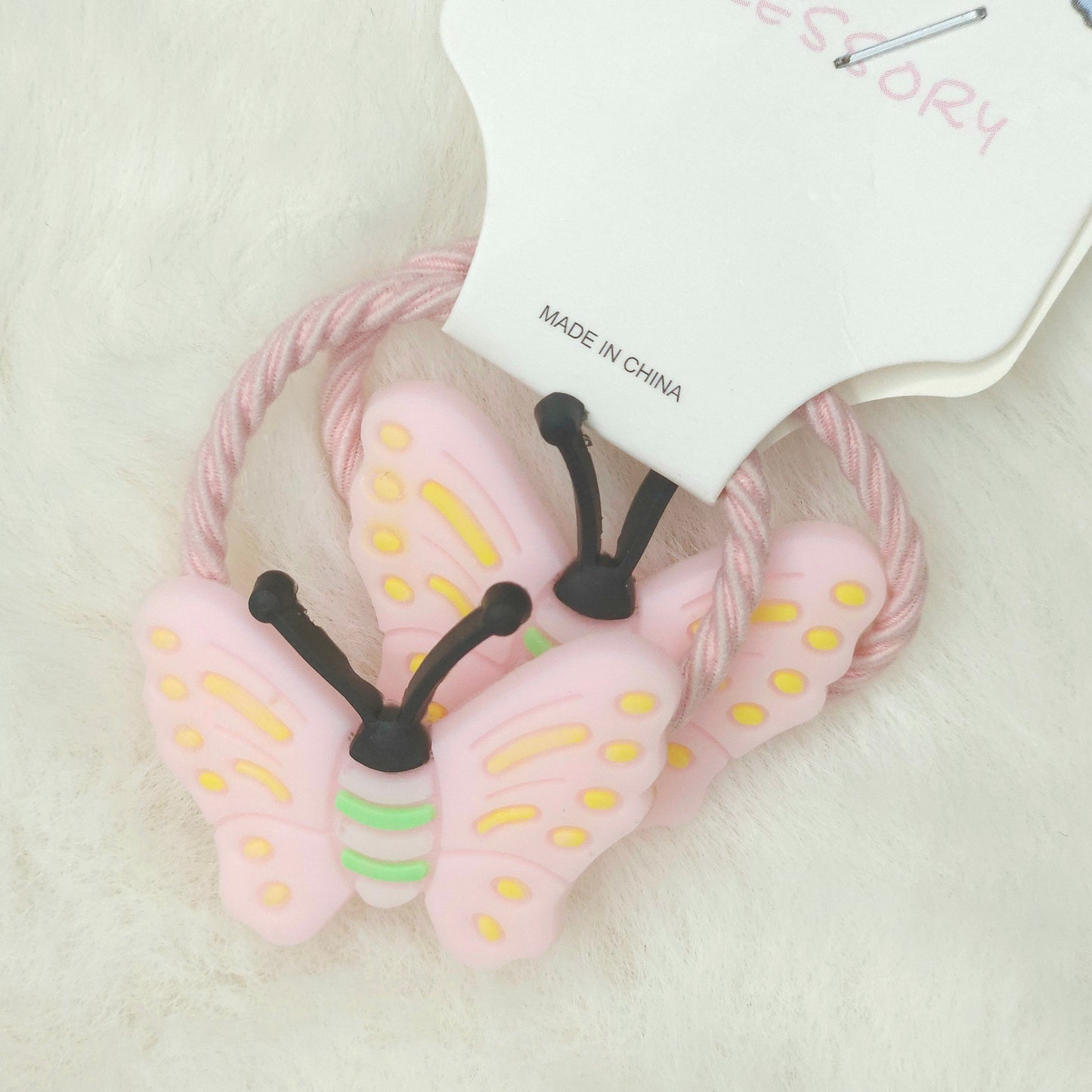 Pink butterfly-shaped hair tie with a visible brand tag on a light background