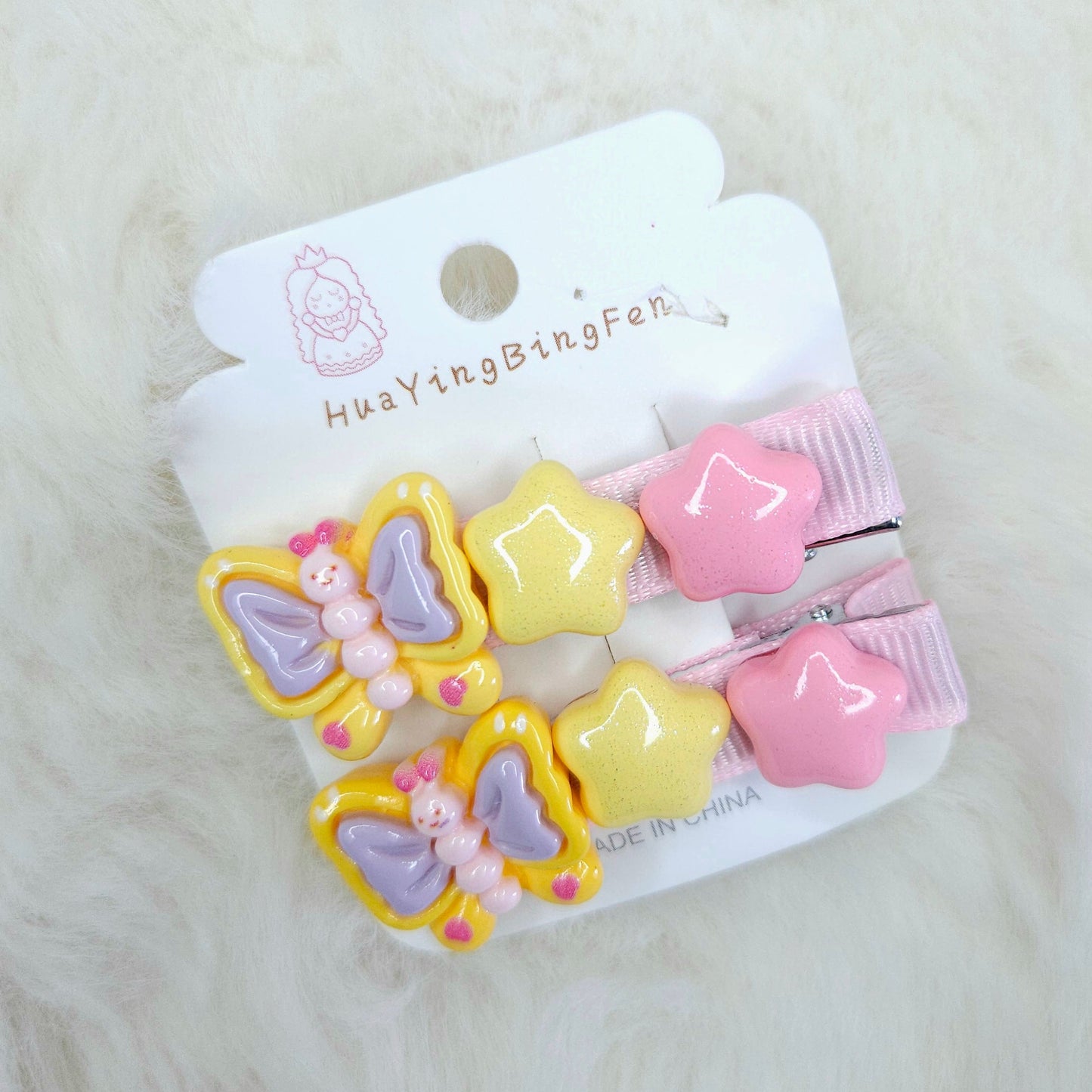 Set of colorful butterfly and star-shaped hair clips on a white card with brand name, on a light gray background.