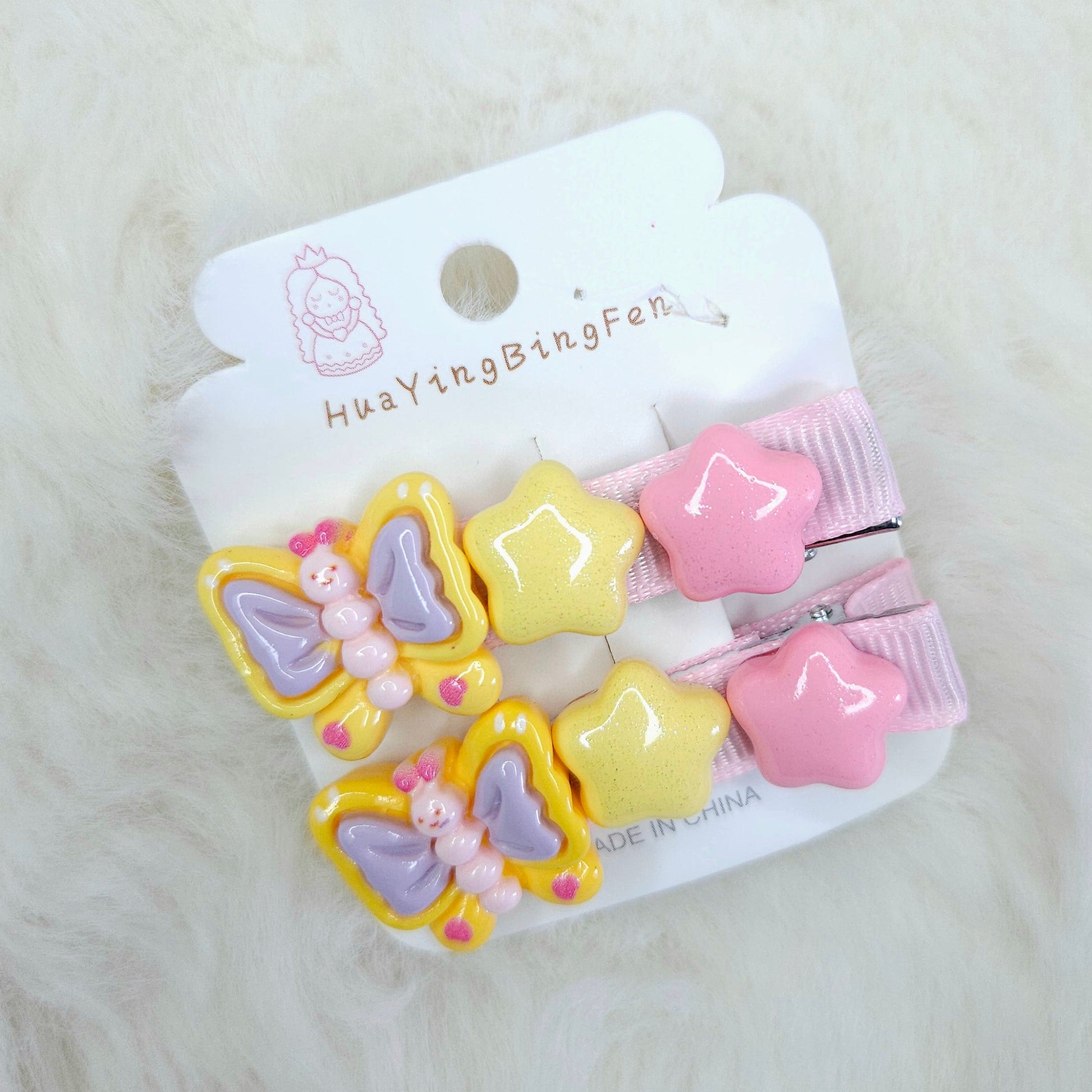 Set of colorful butterfly and star-shaped hair clips on a white card with brand name, on a light gray background.