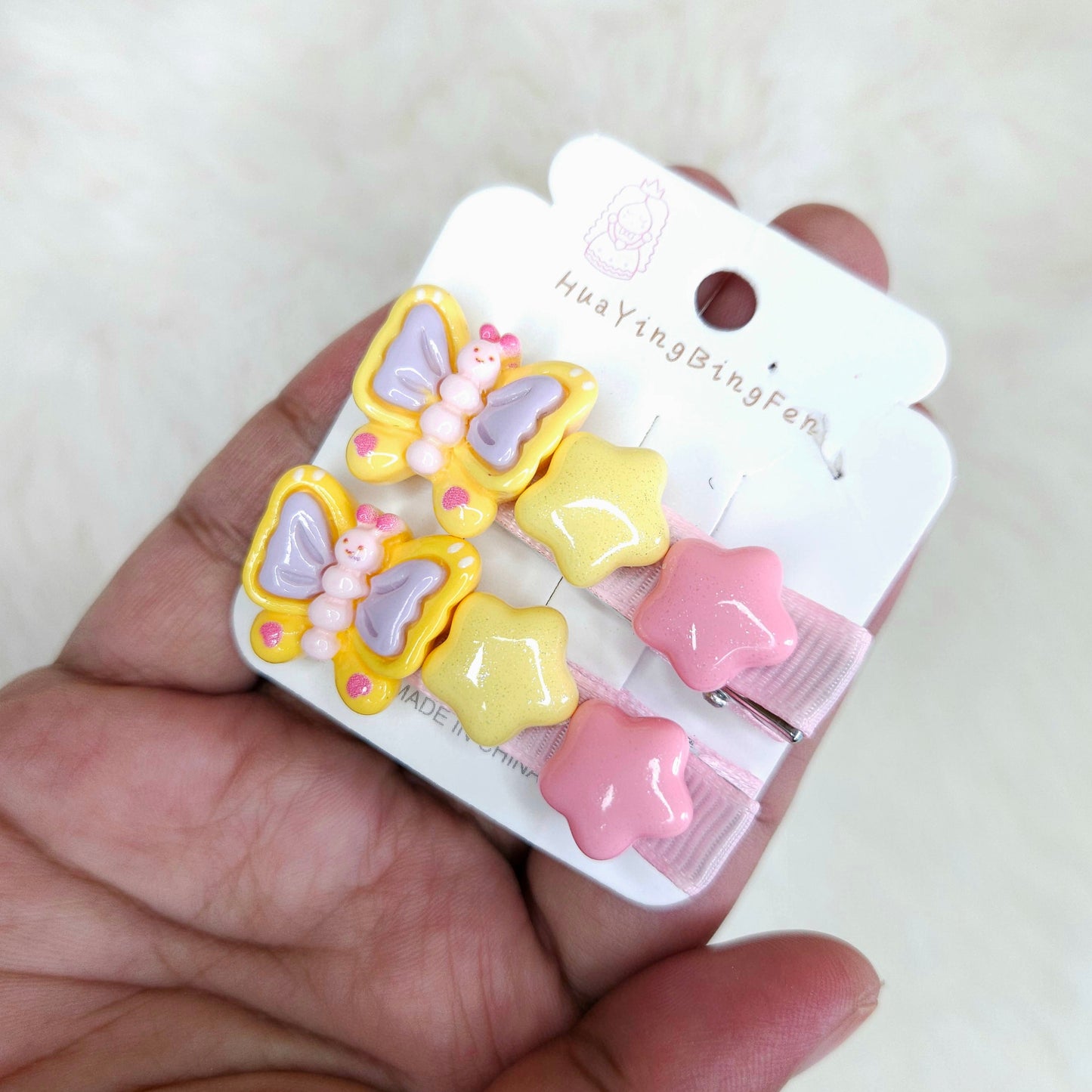 Set of butterfly and star-shaped hair clips on a white card held by a hand.