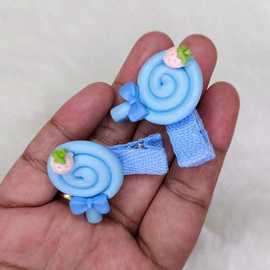 Two blue lollipop-shaped hair clips held in a hand against a light background