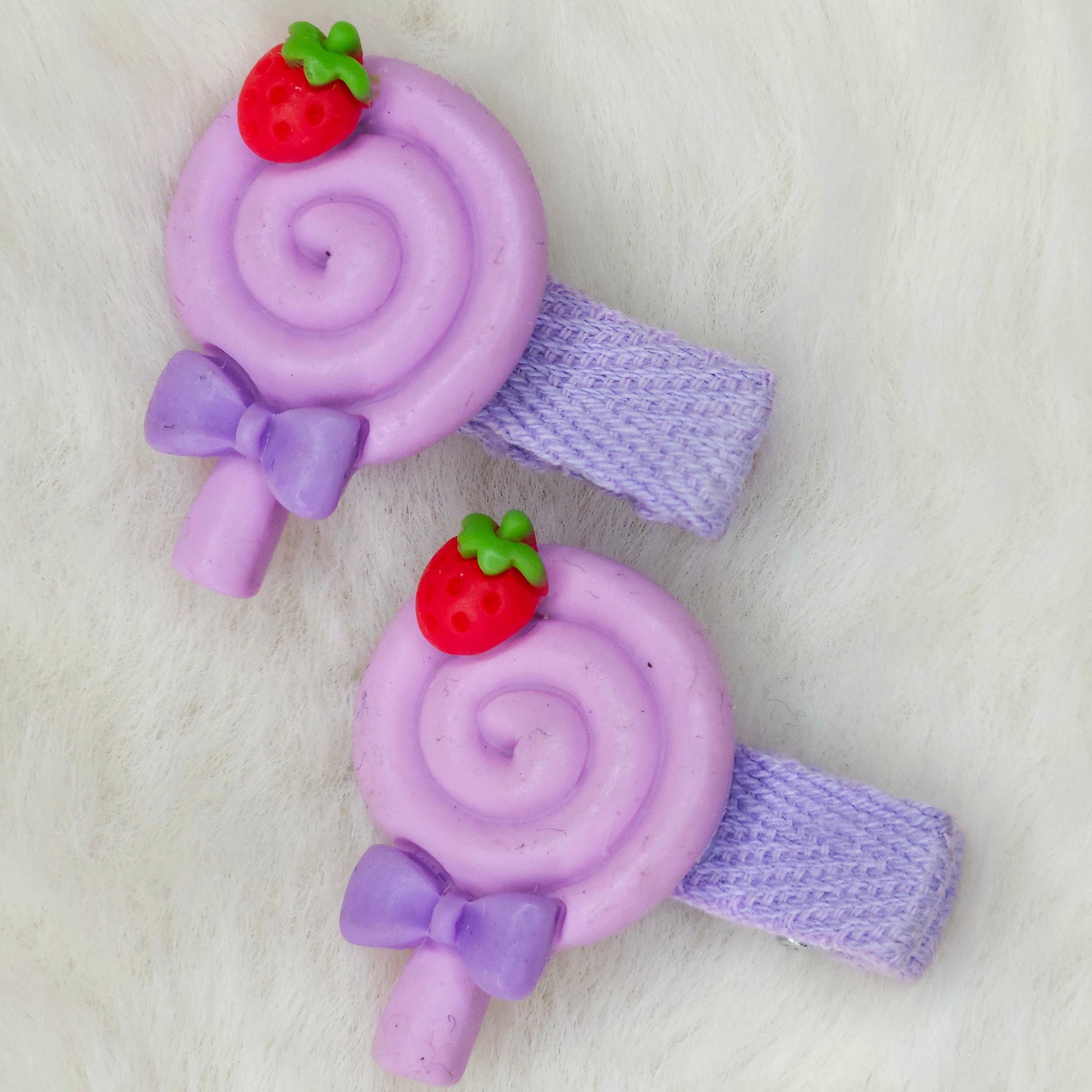 Purple lollipop-shaped hair clips with strawberry decorations on a white background