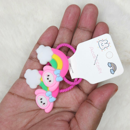 Hand holding a pink hair tie with cloud and rainbow design and a tag on a light background