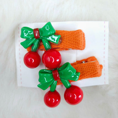 Set of hair clips with red balls, green bows, and orange bases on a white card.