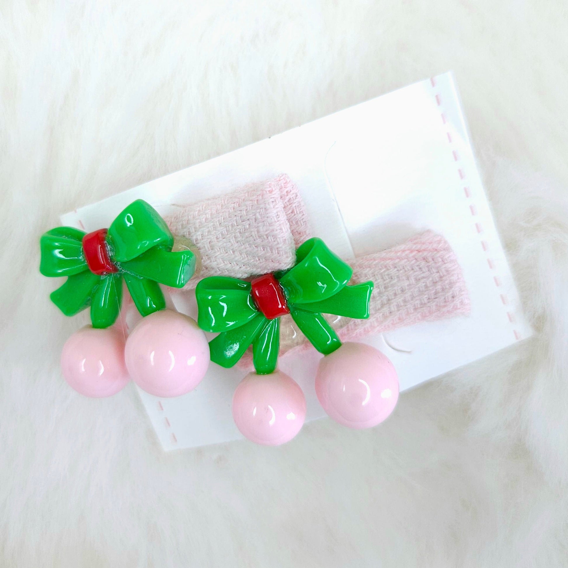 Pair of pink hair clips with green bows on a white background