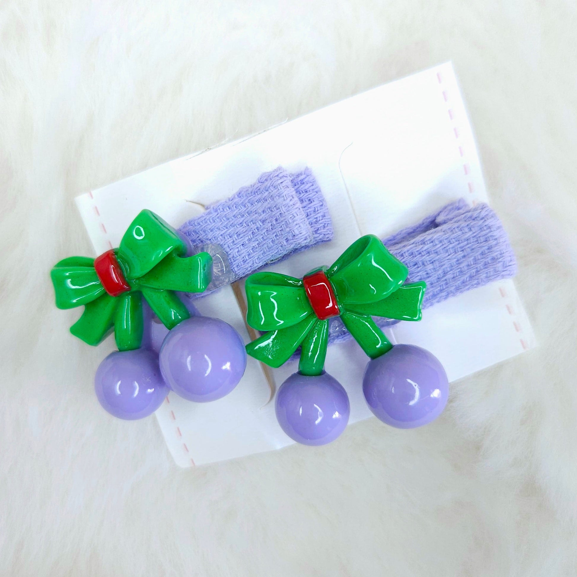 Two purple hair clips with green bows and purple beads on a white background