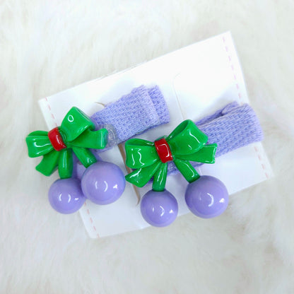 Two purple hair clips with green bows and purple beads on a white background