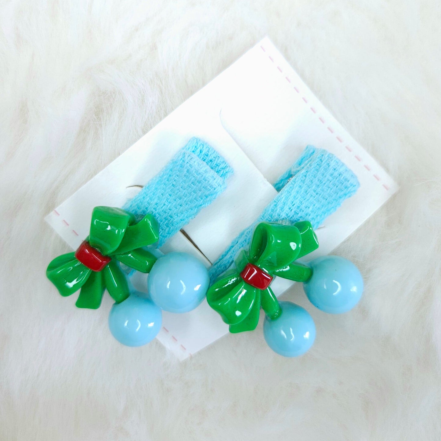 Pair of hair clips with green bows and blue beads on a white background