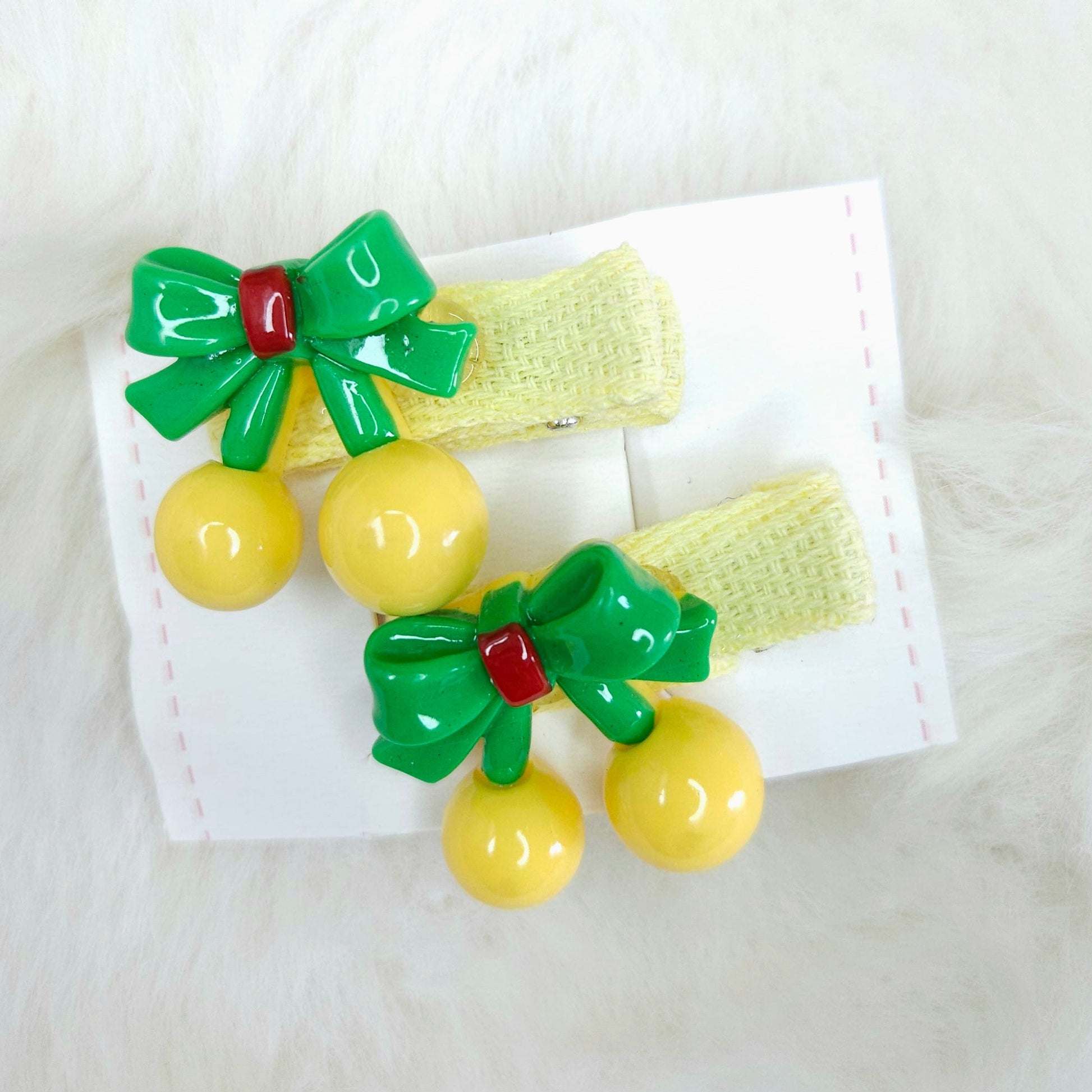 Two hair clips with green bows and yellow beads on a white background