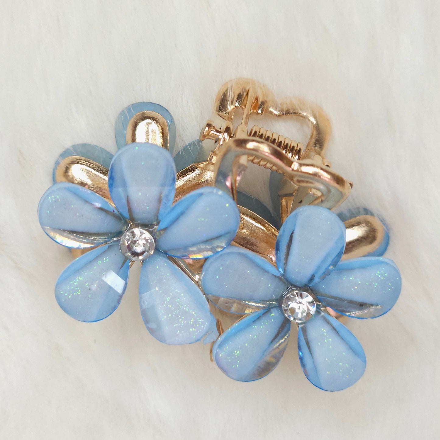 A blue flower-shaped hair clips with gold accents on a light gray background