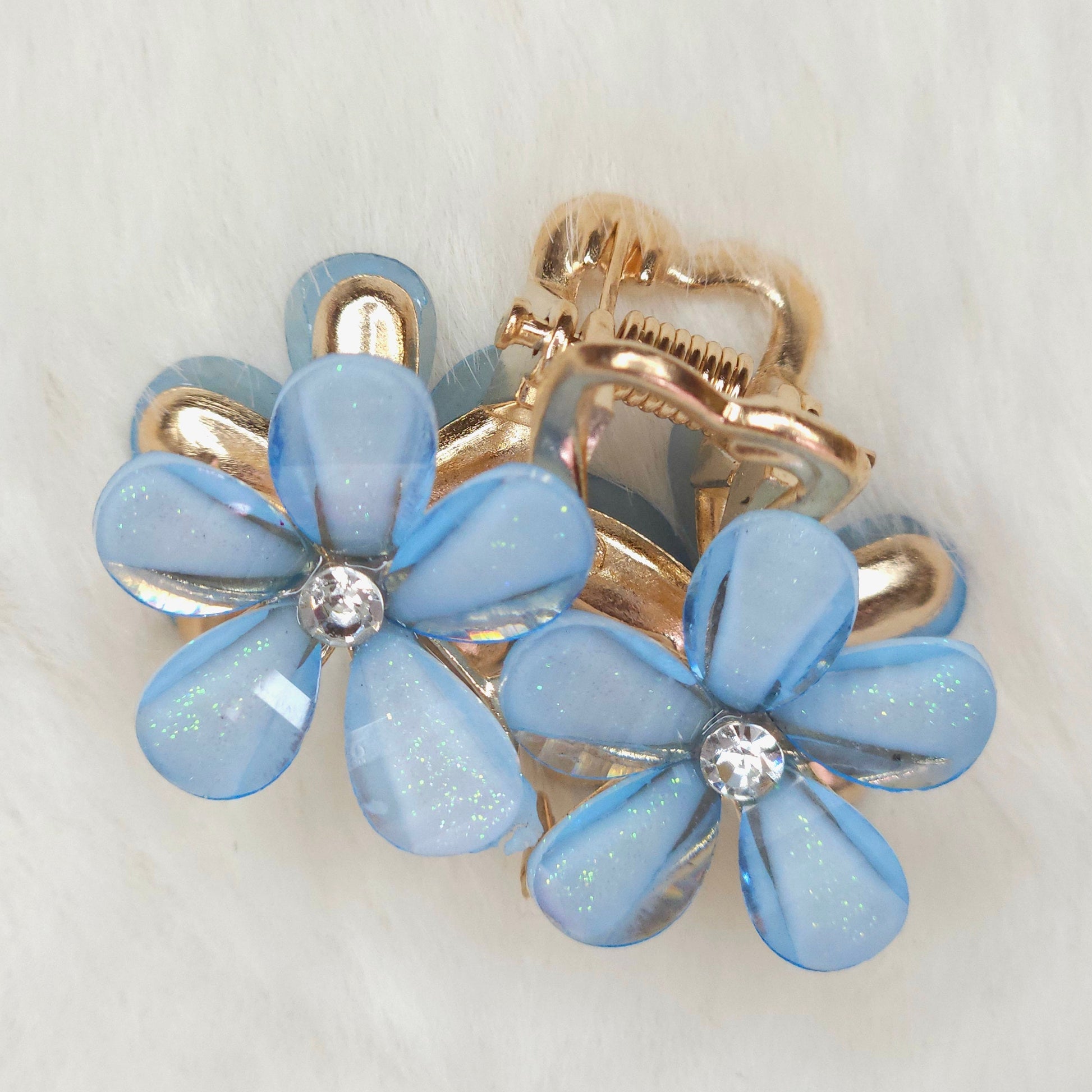 A blue flower-shaped hair clips with gold accents on a light gray background