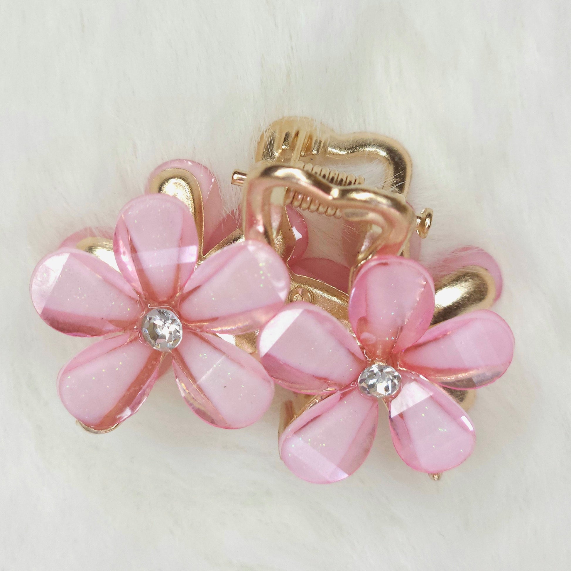 Pink flower-shaped hair clips with gold accents on a light background