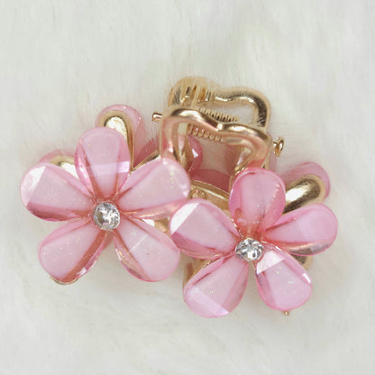 Pink flower-shaped hair clips with gold accents on a light background