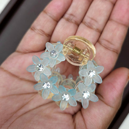 Detailed shot of a pastel blue mini hair clip featuring a cluster of translucent, flower-shaped stones and brilliant micro-rhinestones.