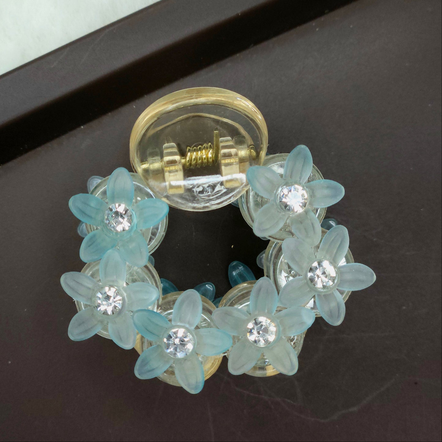 Detailed shot of a pastel blue mini hair clip featuring a cluster of translucent, flower-shaped stones and brilliant micro-rhinestones.