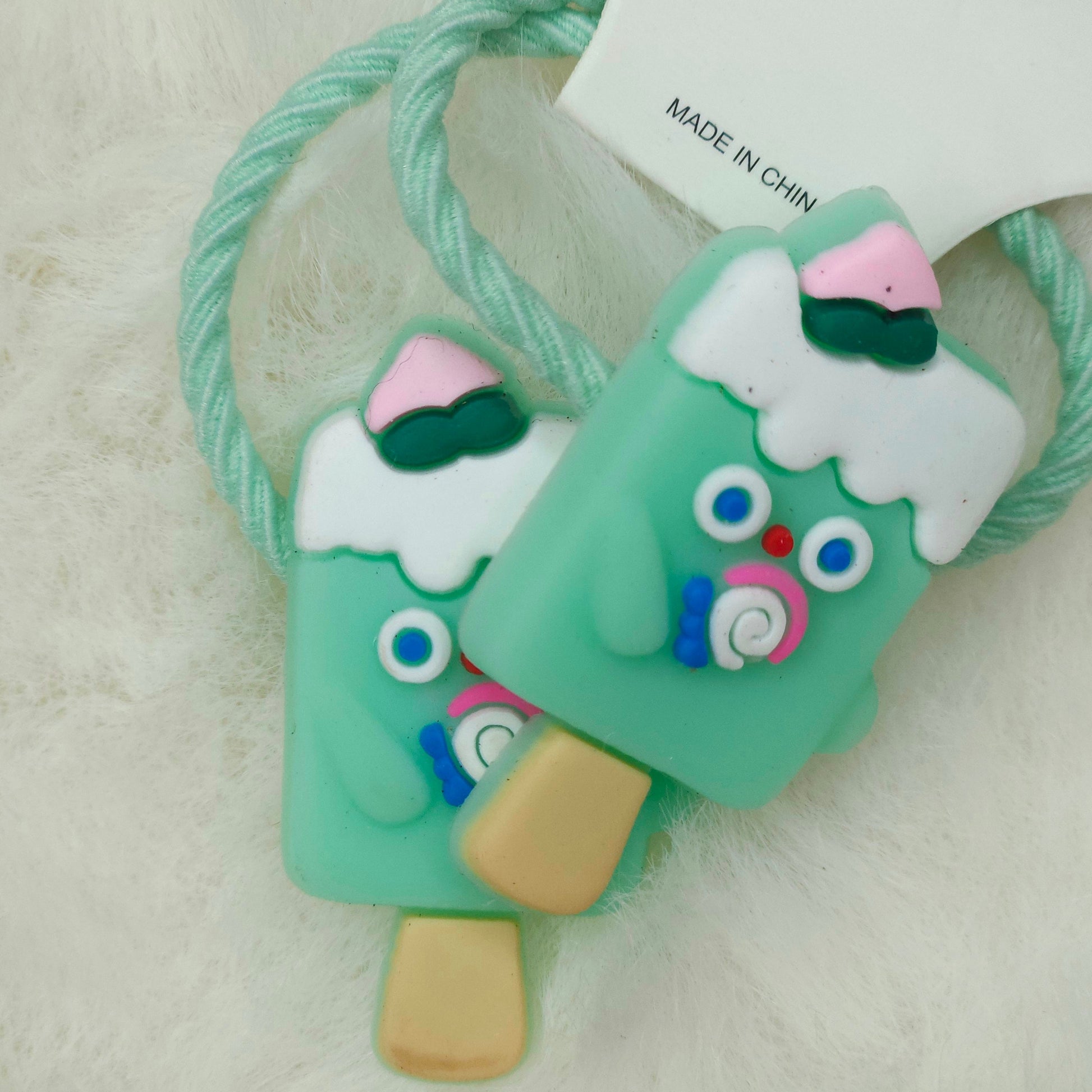 Two green ice cream popsicle-shaped hair ties with colorful designs on a light background.