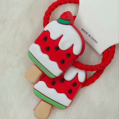 Watermelon-shaped ice cream popsicle hair ties with a red string on a light wooden background.