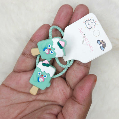 Hand holding a small green ice cream-shaped hair tie with a tag on a light background