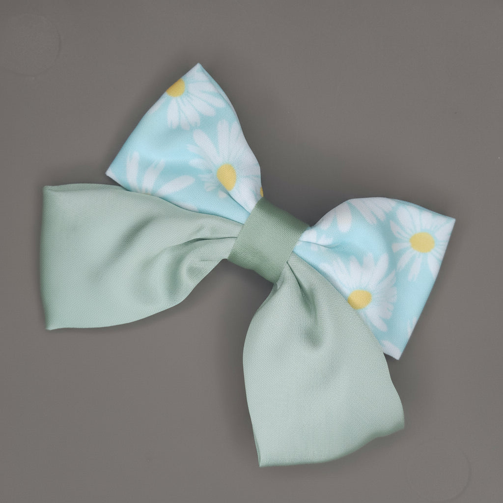 A close-up of a light green satin hair bow adorned with a white daisy floral print, showcasing the fabric's soft sheen.