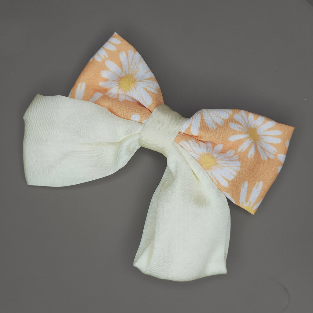 A bright orange satin hair bow, featuring a repeating pattern of white daisy flowers. The bow has a noticeable glossy shine and is secured by a central knot.