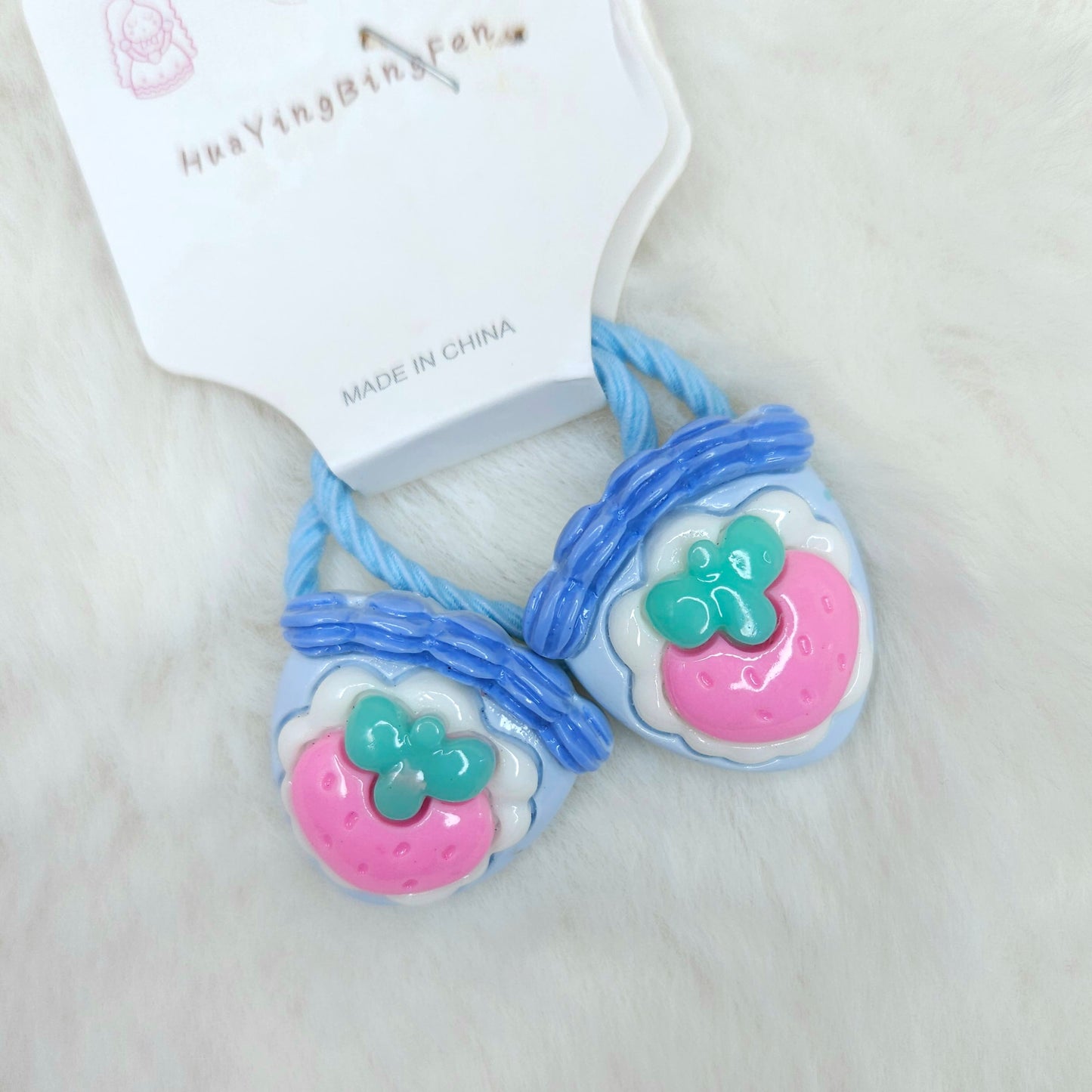 Pair of blue hair ties with pink and green charms on a white background